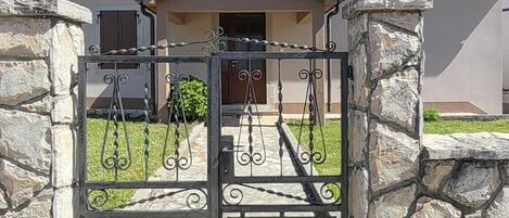 A gated entrance to a house with a stone wall and a metal gate.