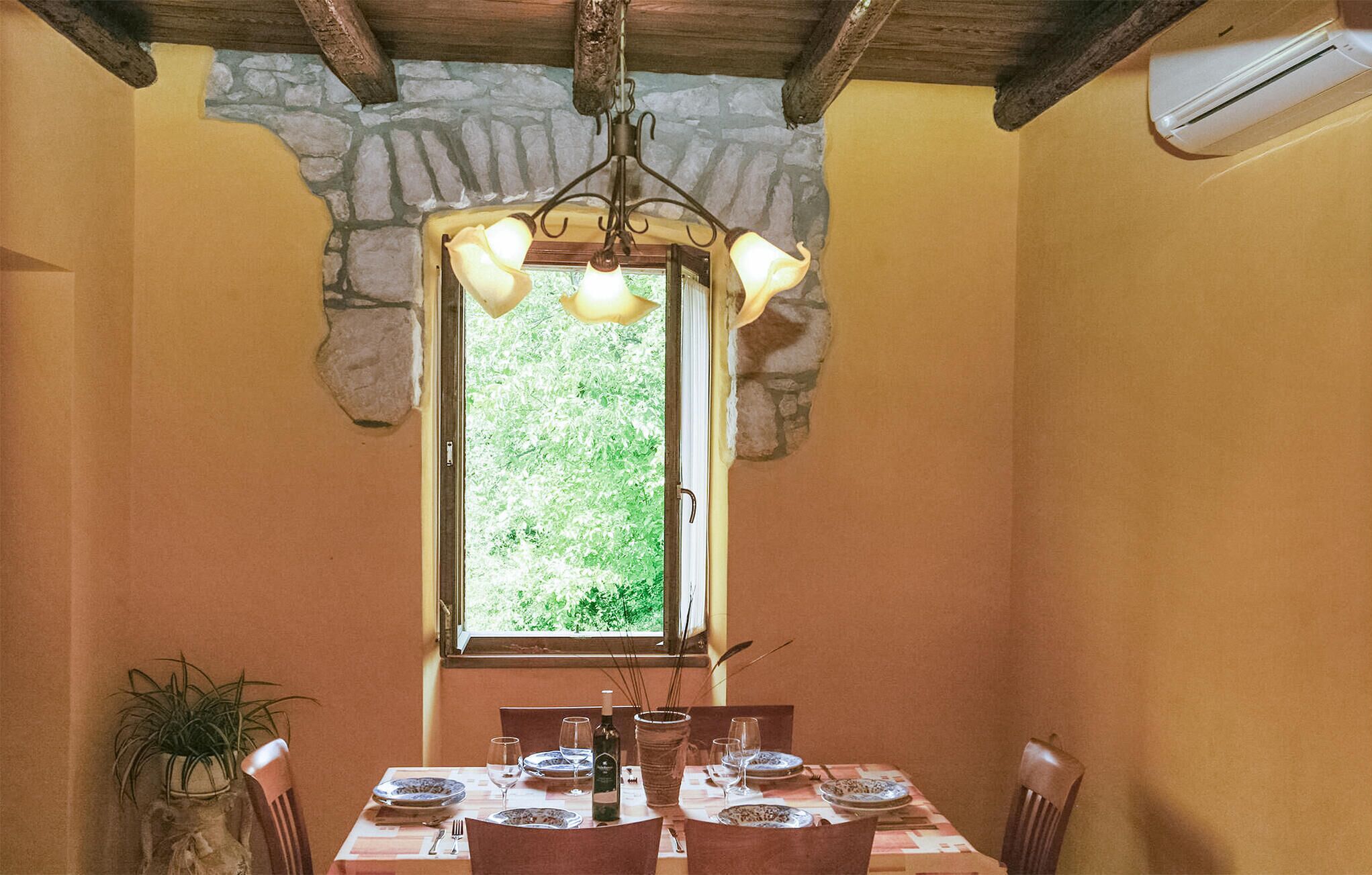 A dining area with a stone-framed window, wooden ceiling beams, and a table set for four with chairs.