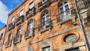 Un immeuble en briques de plusieurs étages, doté de balcons en fer forgé décorés, de grandes fenêtres et d’une porte verte.