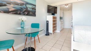 A modern room with a glass table, teal chairs, a flat-screen TV, and a bed. - **Diamond Head, Ocean, and Park Views** (Honolulu)