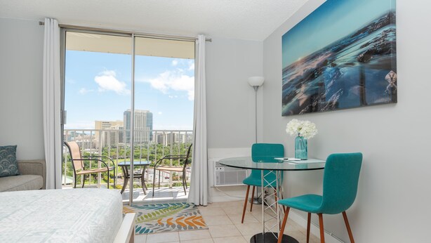 A hotel room with a balcony, a bed, a dining table with chairs, and a painting on the wall. - **Diamond Head, Ocean, and Park Views** (Honolulu)