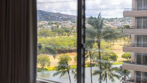A view from a window overlooking a beach with palm trees and a distant town. - Studio with King size bed & Short walk to Beach (Honolulu)