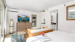 A modern hotel room with a large bed, a flat-screen TV, a wooden cabinet, and a painting of a beach scene. - Studio with King size bed & Short walk to Beach (Honolulu)