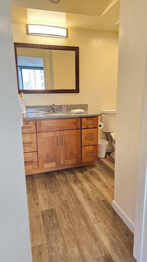 A bathroom with wooden cabinets, a granite countertop, a mirror, and a toilet.