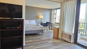 A hotel room with a bed, a desk, a chair, a TV, and a window with curtains. - Beautiful Waikiki Banyan (Honolulu)