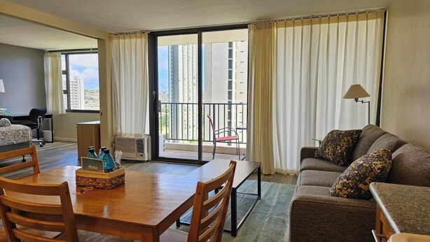 A hotel room with a dining area, a sofa, and a balcony with curtains. - Beautiful Waikiki Banyan (Honolulu)