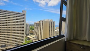A view from a window overlooking high-rise buildings, a clear sky, and a distant body of water. - Beautiful Waikiki Banyan (Honolulu)
