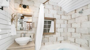 A bathroom with a white bathtub, a sink, and a shower curtain. - Centre St. Cottage | 1/1, King Bed, Mini Kitchen (Fredericksburg)