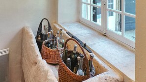 Esquina de una habitación con una ventana, un alféizar de piedra y dos cestas de mimbre con botellas.