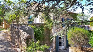 Un patio exterior con muros de piedra, una pequeña reja y un edificio con tejado de baldosas al fondo.