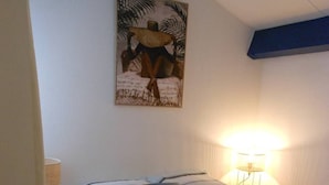 Un dormitorio con cama, mesita de noche, lámpara y un cuadro en la pared.