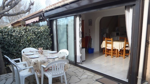 Un área de comedor al aire libre con un patio de baldosas de piedra, sillas de plástico blancas y una mesa dispuesta para dos personas.