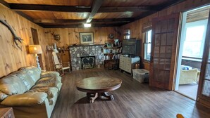 A cozy cabin interior with a wooden floor, a round dining table, a sofa, a fireplace, and a television. - Lakefront house with land dock (Conneaut Lake)