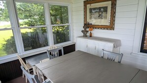 A dining area with a large table and chairs, a window with a view of greenery, and a wooden ceiling. - Lakefront house with land dock (Conneaut Lake)