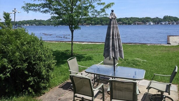 An outdoor patio with a table and chairs, a covered umbrella, and a view of a lake with boats. - Lakefront house with land dock (Conneaut Lake)
