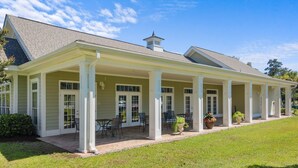 A covered patio with outdoor seating, a brick pathway, and a grassy lawn.