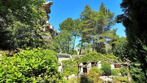 Una casa de piedra rústica rodeada de abundante vegetación y un cielo azul despejado.
