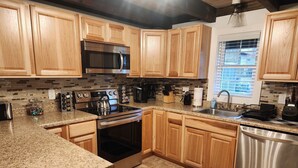 Una cocina moderna con gabinetes de madera, encimeras de granito, electrodomésticos de acero inoxidable y una ventana que proporciona luz natural.