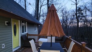 Una terraza de madera con una mesa y sillas, una sombrilla y una casa con puerta verde.