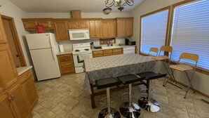 Una cocina compacta con armarios de madera, un refrigerador blanco, un microondas y una estufa. Hay una mesa de comedor con cuatro sillas y una araña colgante.