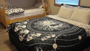 Una habitación con una cama litera, una cama grande con colcha estampada, y una ventana con persianas.