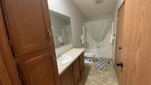 Baño con tocador de madera, lavamanos, inodoro y ducha con cortina.