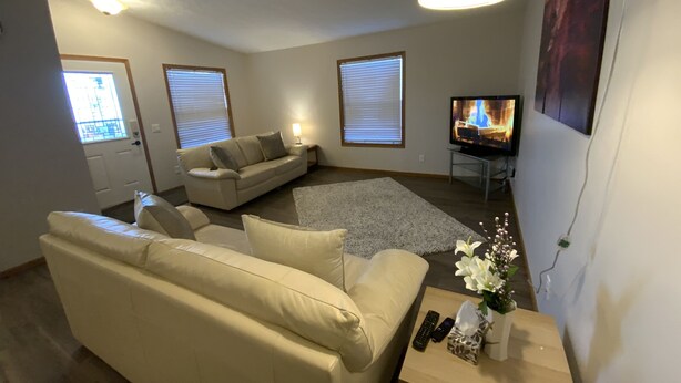 Una sala de estar con un sofá color beige, una mesa de centro con un jarrón de flores, un televisor y una chimenea.