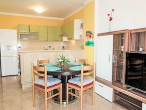 A compact kitchen with a dining table, chairs, a refrigerator, and a TV cabinet.