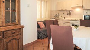 A compact kitchen with a dining area, featuring a cabinet with glass doors, a sofa, and a table with chairs. - Victory by Interhome (Labin)