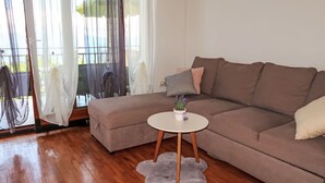 A modern living room with a brown sofa, a round white coffee table with a plant, and sheer curtains on the windows. - Victory by Interhome (Labin)