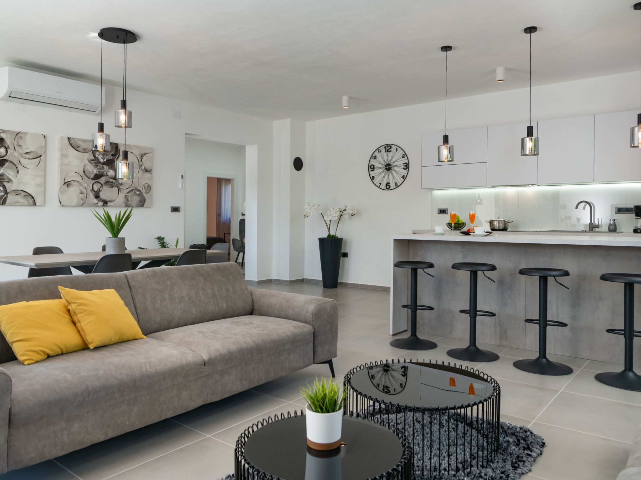 A modern living room with a grey sofa, a round coffee table, and a kitchen area with a bar stool set.