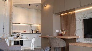 Una cocina moderna con electrodomésticos integrados, un comedor con mesa y sillas blancas, y un televisor montado en una pared de mármol.