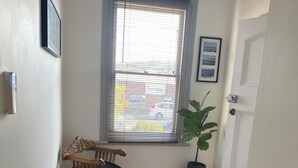 A hallway with wooden flooring, a window with blinds, a door, a small chair, and a potted plant. - Comfy home within walking distance to beach, restaurants and Blunderstone area. (Bellerive)