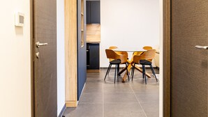 A hallway with two wooden doors, a dining area with a table and chairs, and a kitchen area with cabinets and a refrigerator. - The Little Paradise lake view (Annecy)