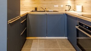 A modern kitchen with dark cabinets, a wooden backsplash, and a tiled floor. - The Little Paradise lake view (Annecy)