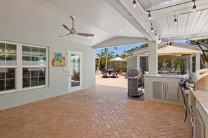 A spacious patio with a grill and outdoor seating, a ceiling fan, and a view of the outdoors. - Water's Edge: Dog Friendly, Canal Front, Dock & Pool & Spa (Anna Maria)