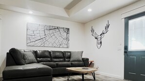 A modern living room with a black leather sofa, a round coffee table, and a large abstract painting on the wall.