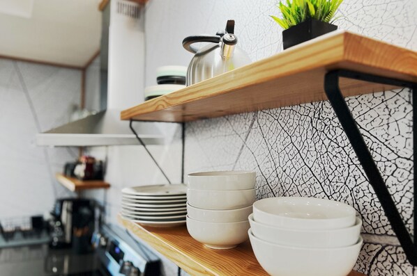 Una cocina con un estante de madera que sostiene cuencos y un hervidor.
