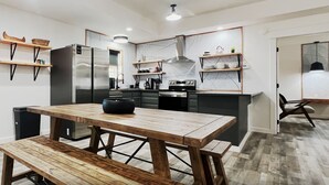 A modern kitchen with a wooden table and bench, built-in appliances, and open shelving.