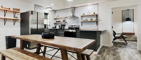 Una cocina moderna con una mesa y banco de madera, electrodomésticos integrados y estantes abiertos.