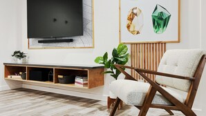 A modern living room with a flat-screen TV mounted on the wall, a wooden entertainment unit with books and decorative items, a white cushioned armchair, and a large green plant.