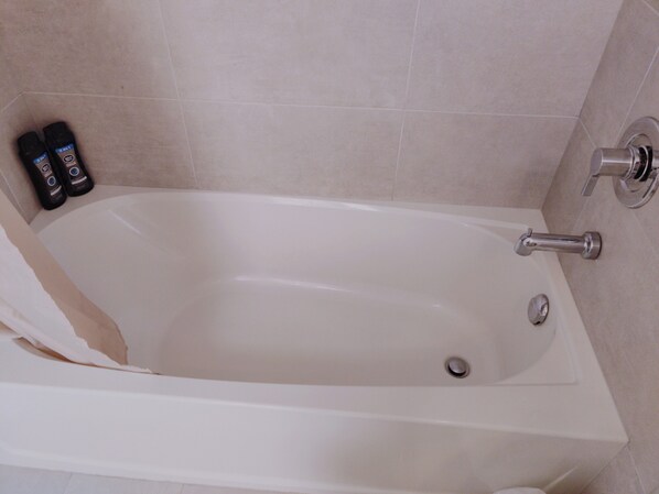 Valkoinen kylpyamme, jossa on suihkupää, ja seinällä on kaksi pulloa hygieniatuotteita.