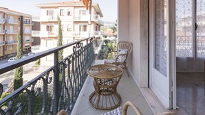 Ein Balkon mit Korbmöbeln, Blick auf benachbarte Gebäude und eine Tür mit gemusterten Vorhängen.