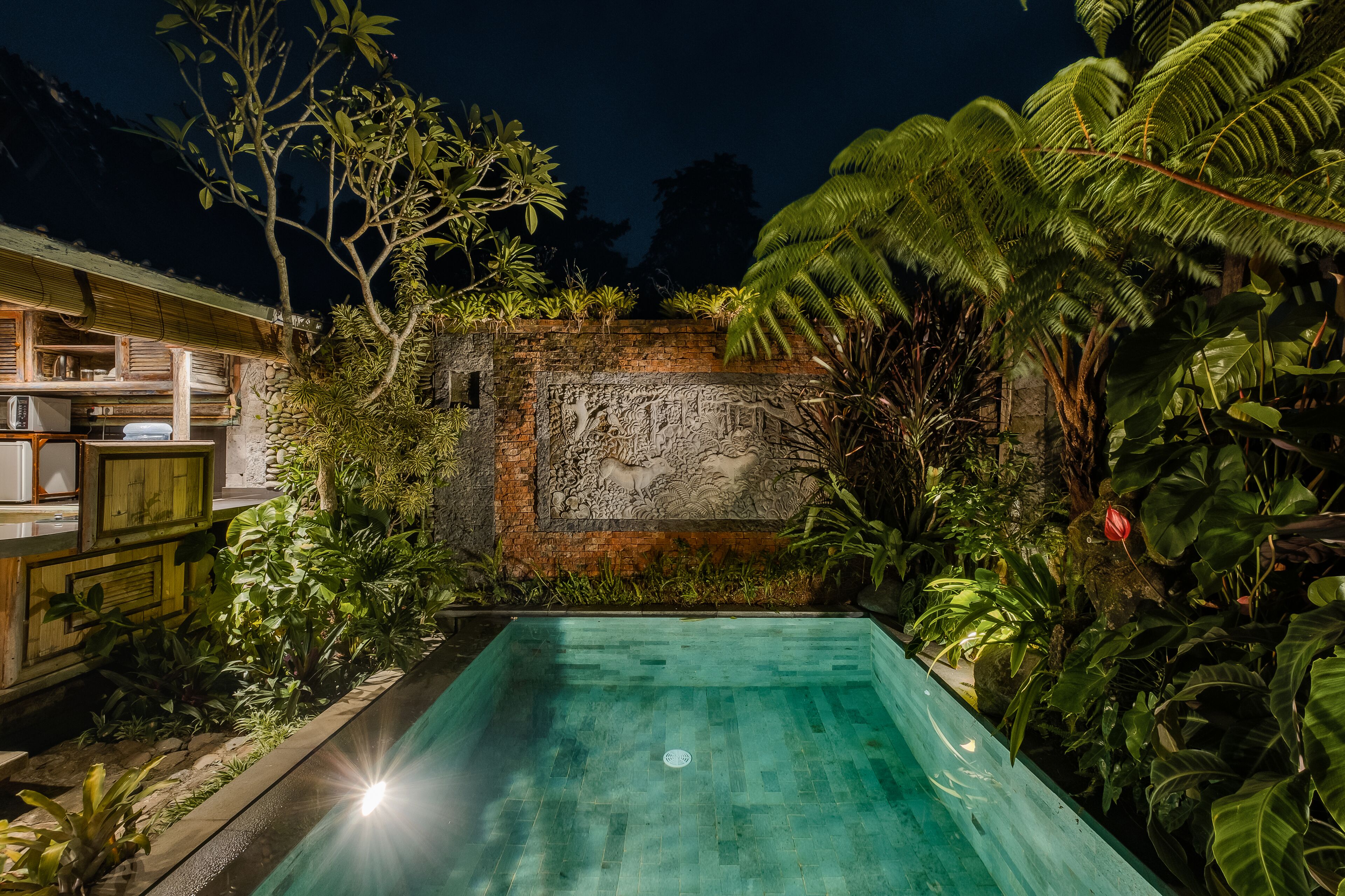 A swimming pool surrounded by lush greenery and a stone wall with carvings.