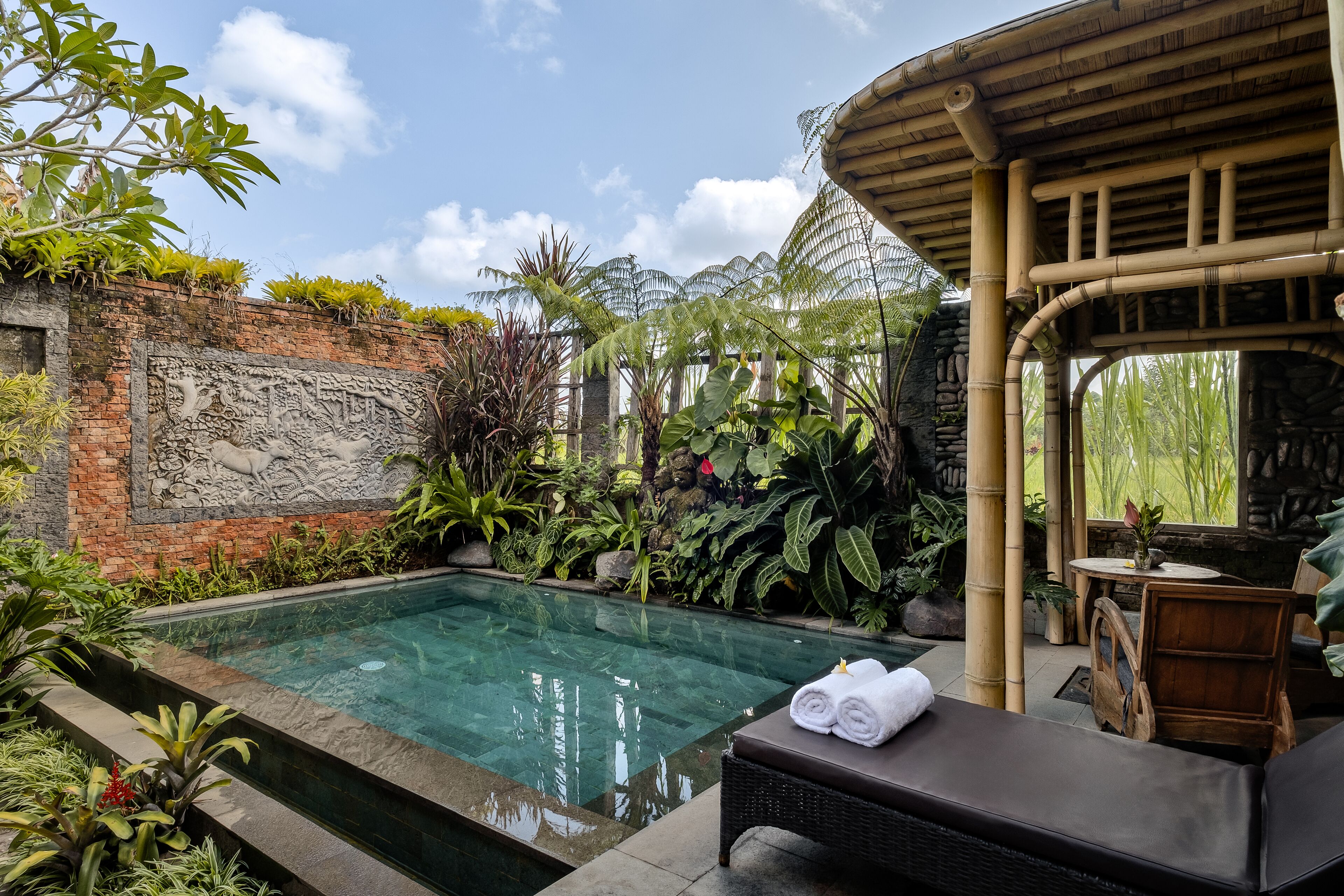 A pool area with a clear water surface, surrounded by lush greenery and a stone wall with carvings.