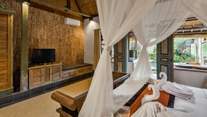 Een kamer met een bed onder een hemelbed, een televisie op een houten kast, en uitzicht op groen buiten.