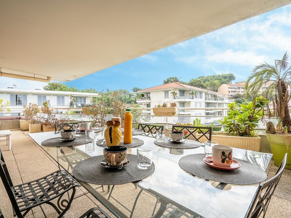 A glass-top table with chairs, a bottle, and a cup on a balcony overlooking a residential area with houses and greenery.