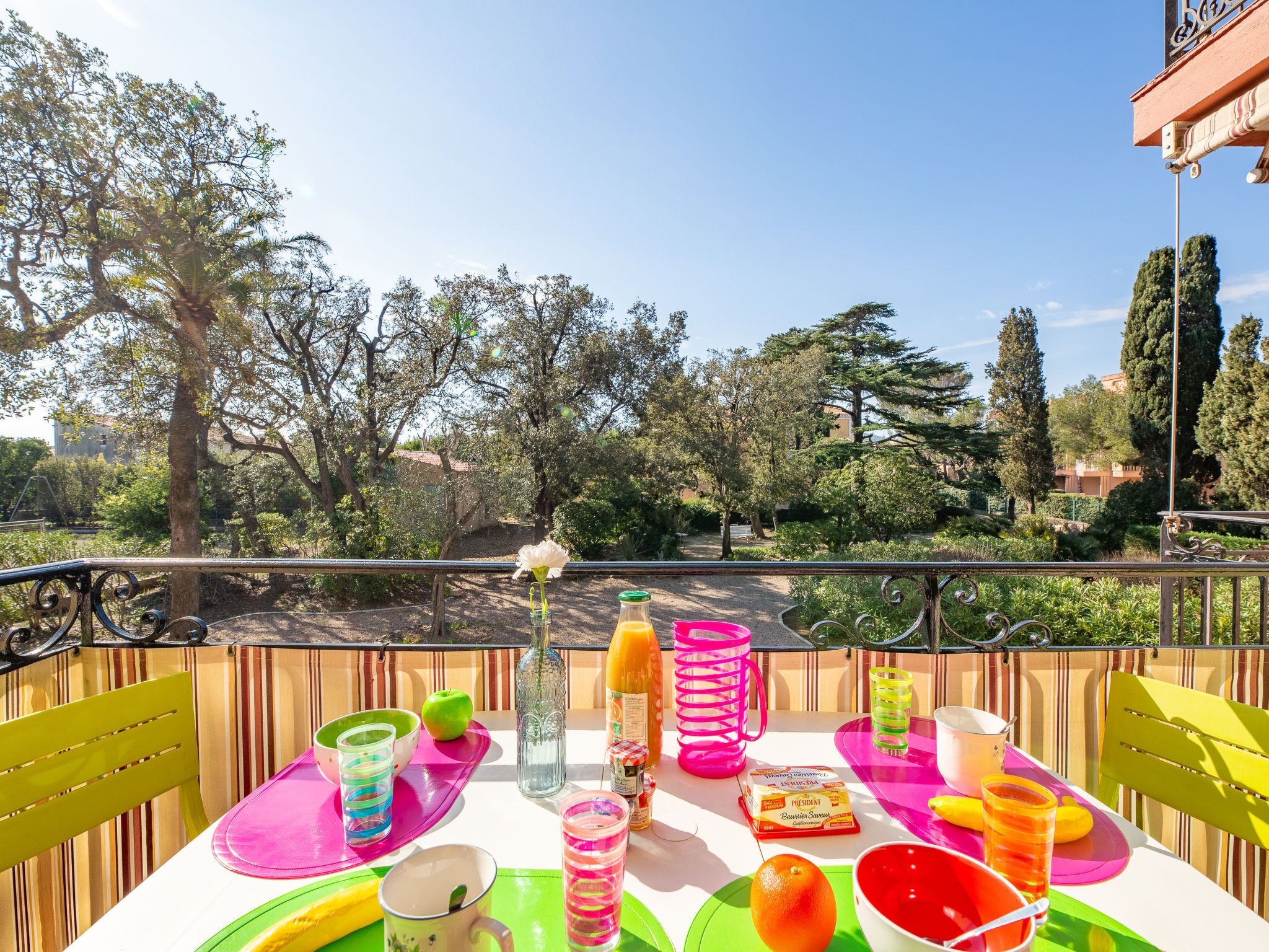 A balcony with a table set for a meal, surrounded by greenery and trees.