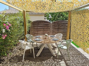 Ein runder Tisch mit vier Stühlen auf einer Holzterrasse unter einem gelb-vernetzten Pergola.
