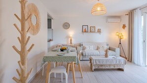 A modern living room with a dining area, featuring a wooden tree sculpture, a round wall hanging, a dining table with chairs, a sofa, a floor lamp, and a ceiling light fixture.